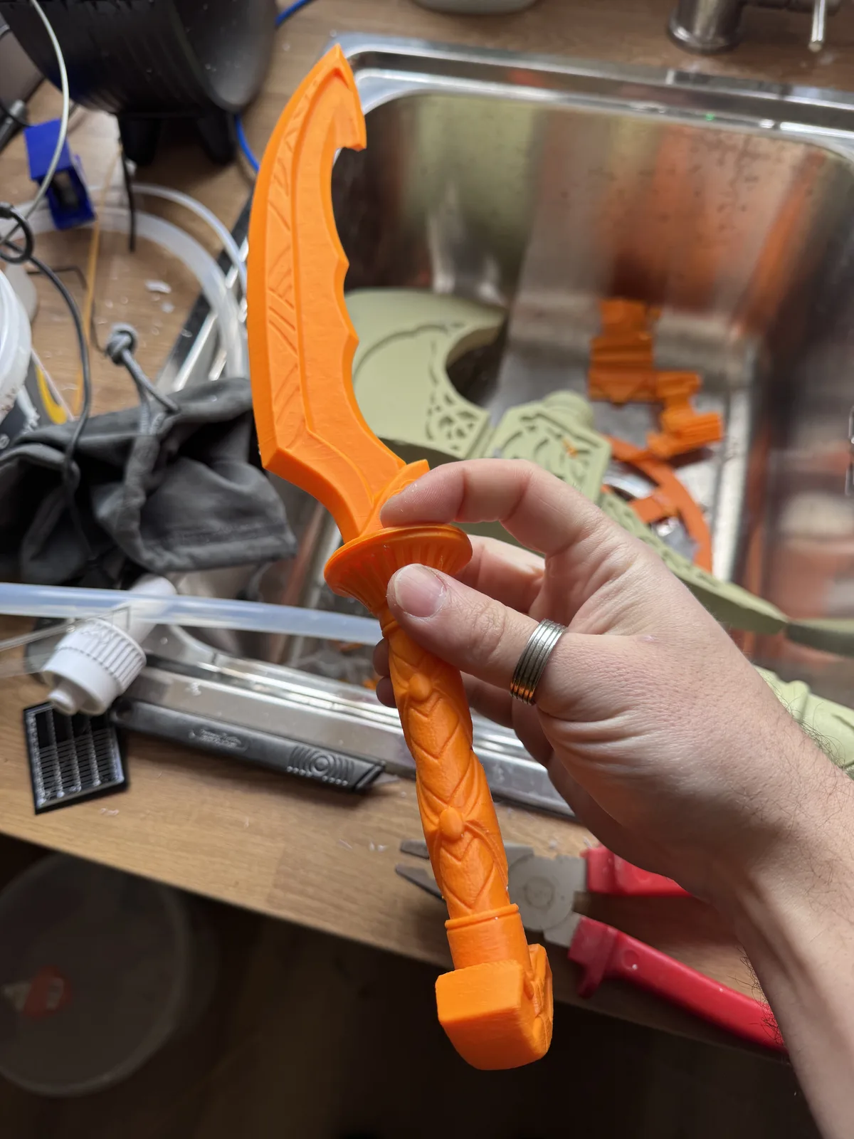 Hand holding an orange 3D-printed dagger handle in the workshop