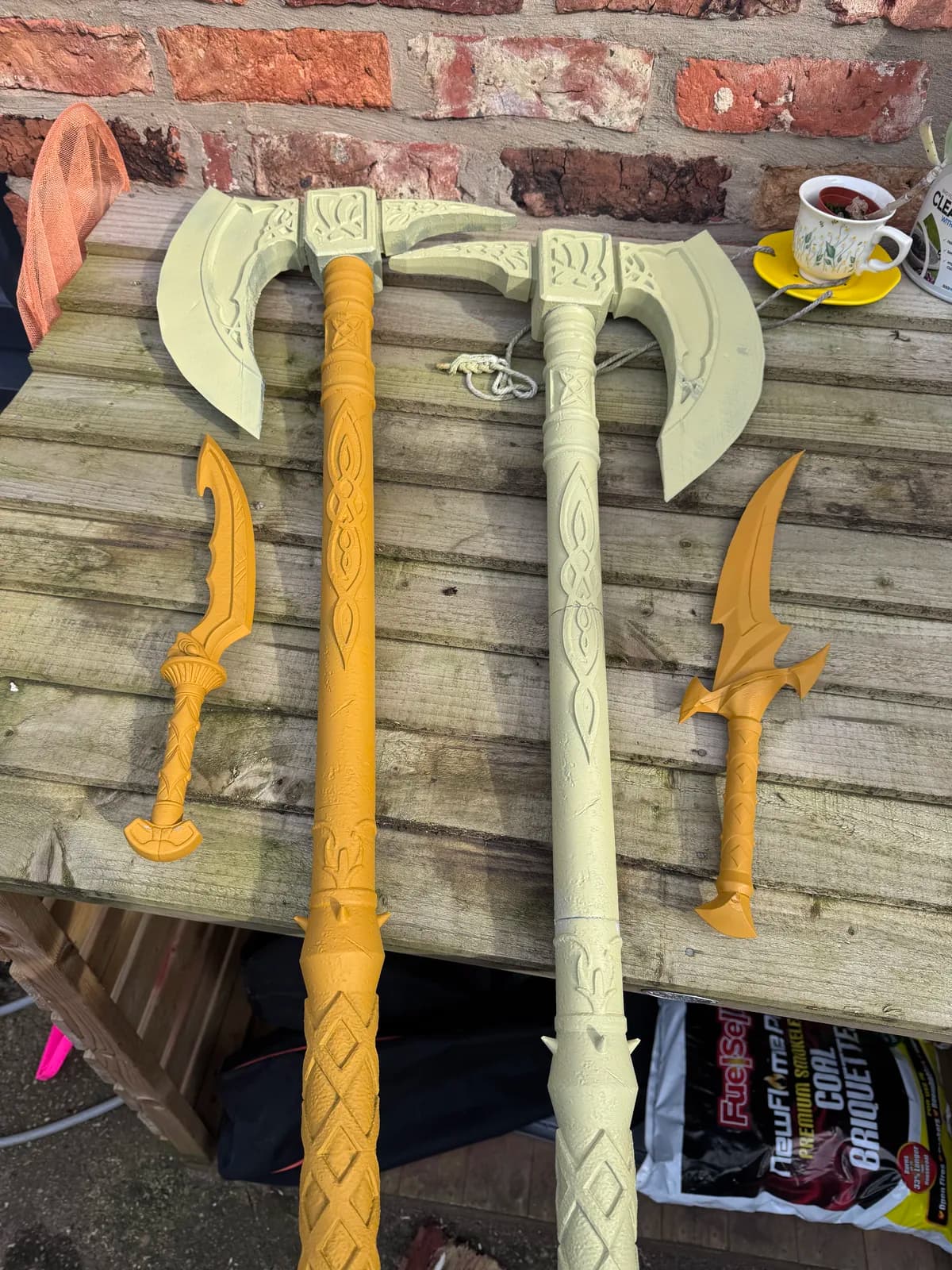 Unpainted fantasy axes and smaller weapon parts laid out on a bench