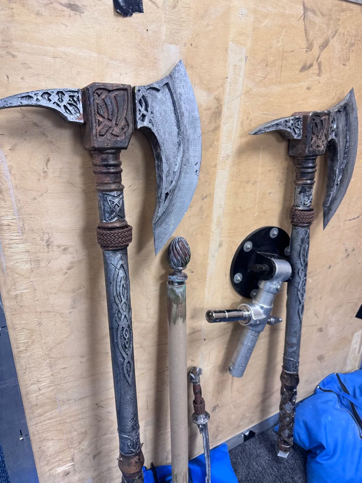 Two painted fantasy battle axes leaning against a workshop wall