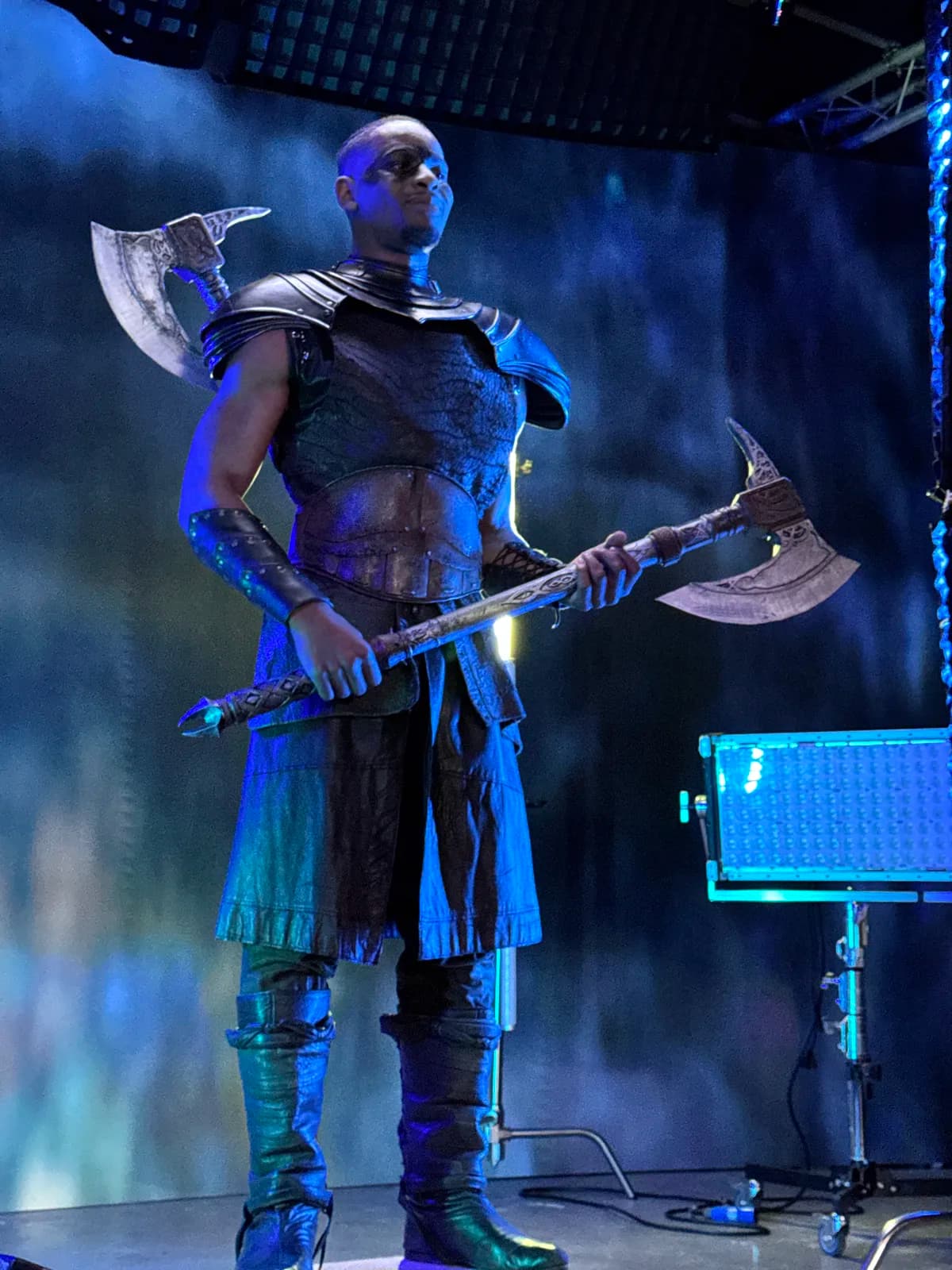 Armoured actor holding a battle axe on a blue-lit stage