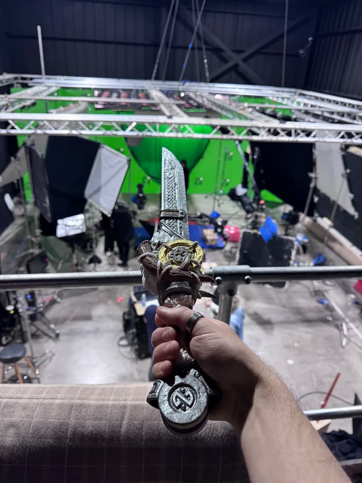 Hand holding an ornate pendant beside a green-screen production stage