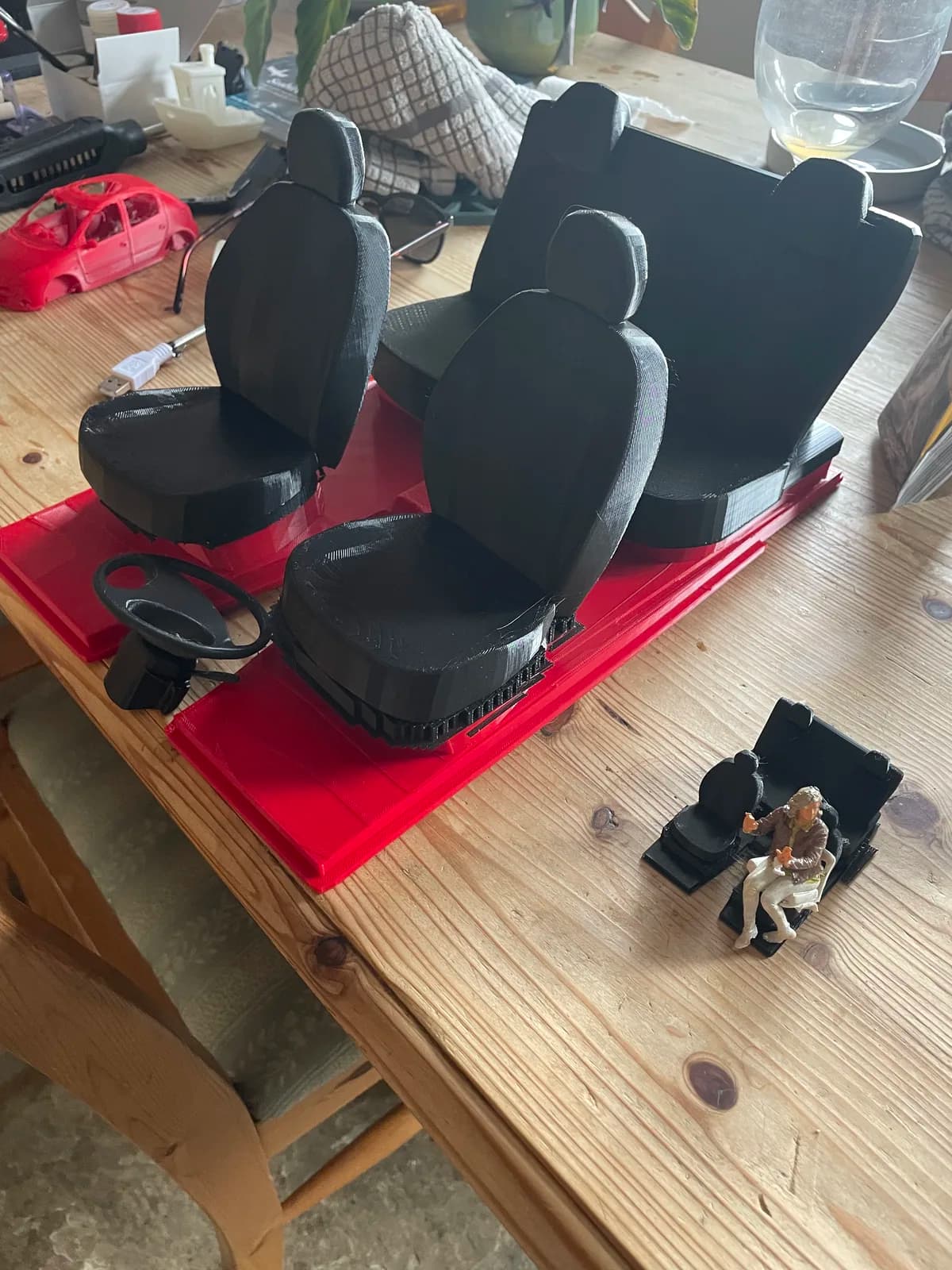 Miniature car seats and interior components arranged on a red base in the workshop