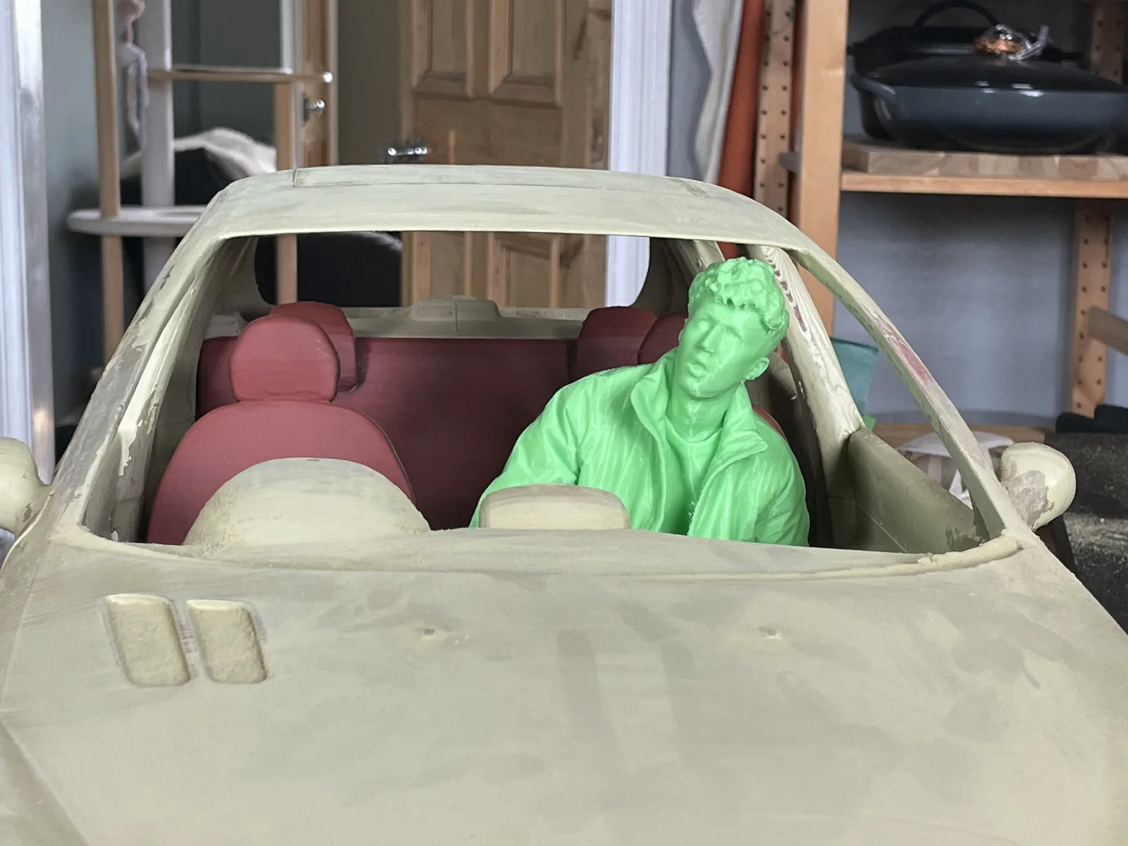 Unfinished miniature car interior with seated figures and a pale body shell