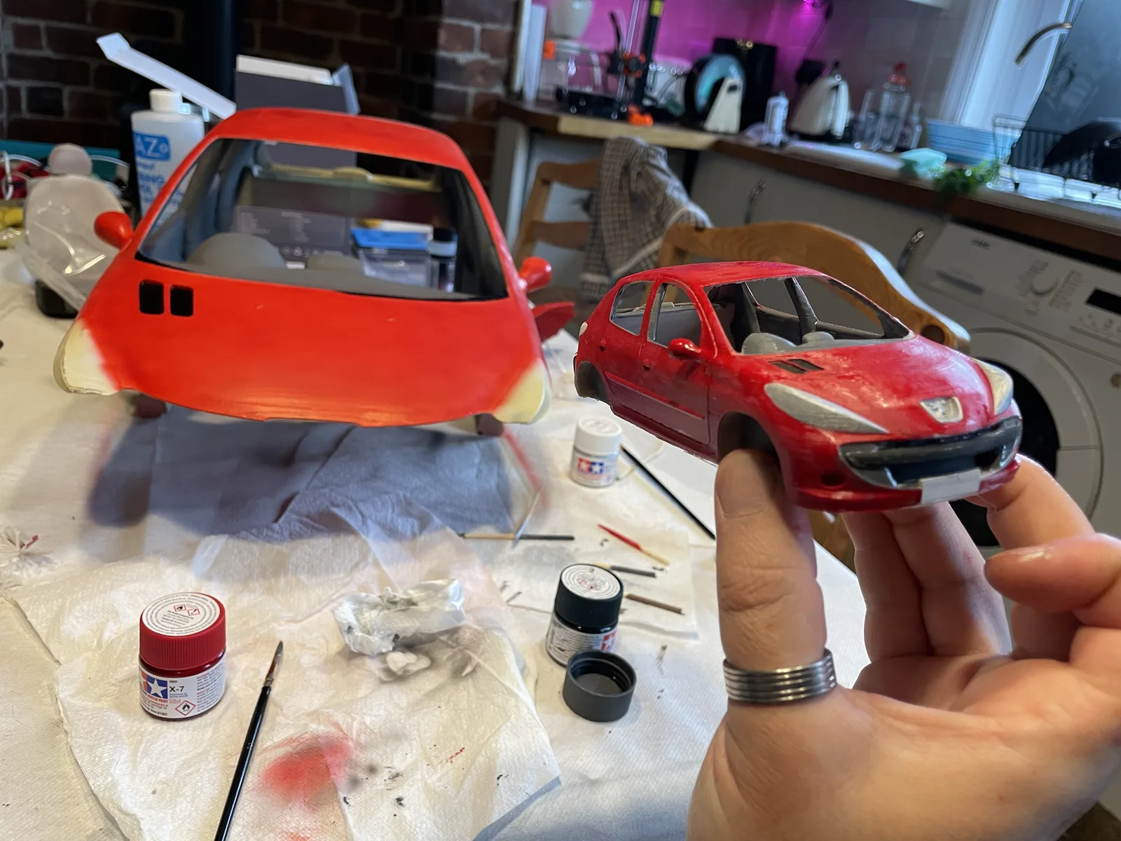 Small painted red model car held beside a larger matching car body