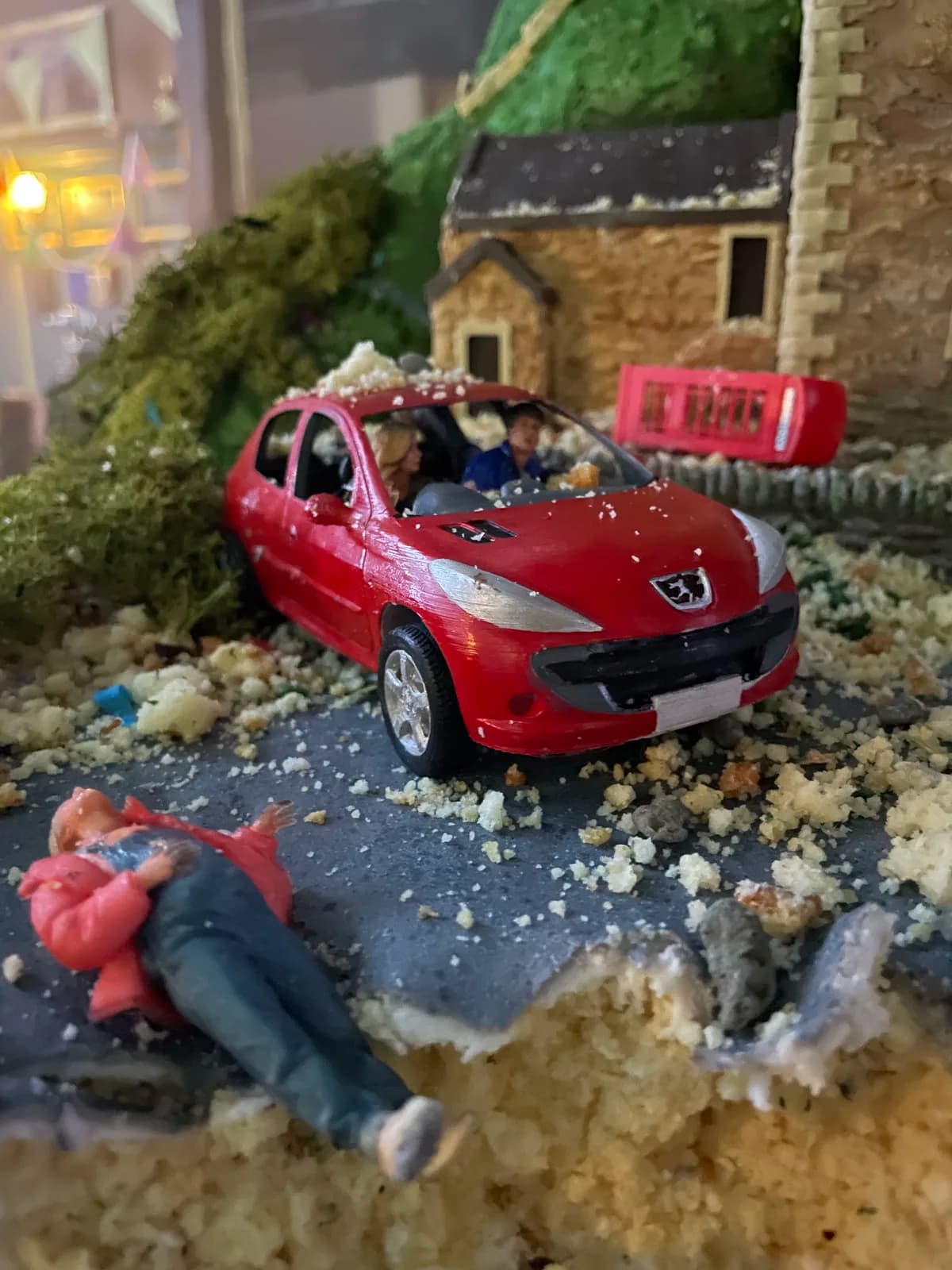 Red model car placed in a miniature landscape with a cottage and figures