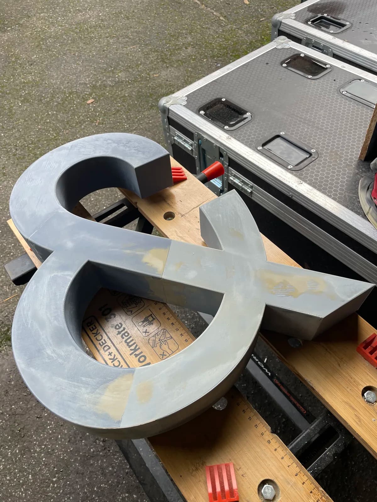 Grey ampersand prop with filled joints resting beside a flight case