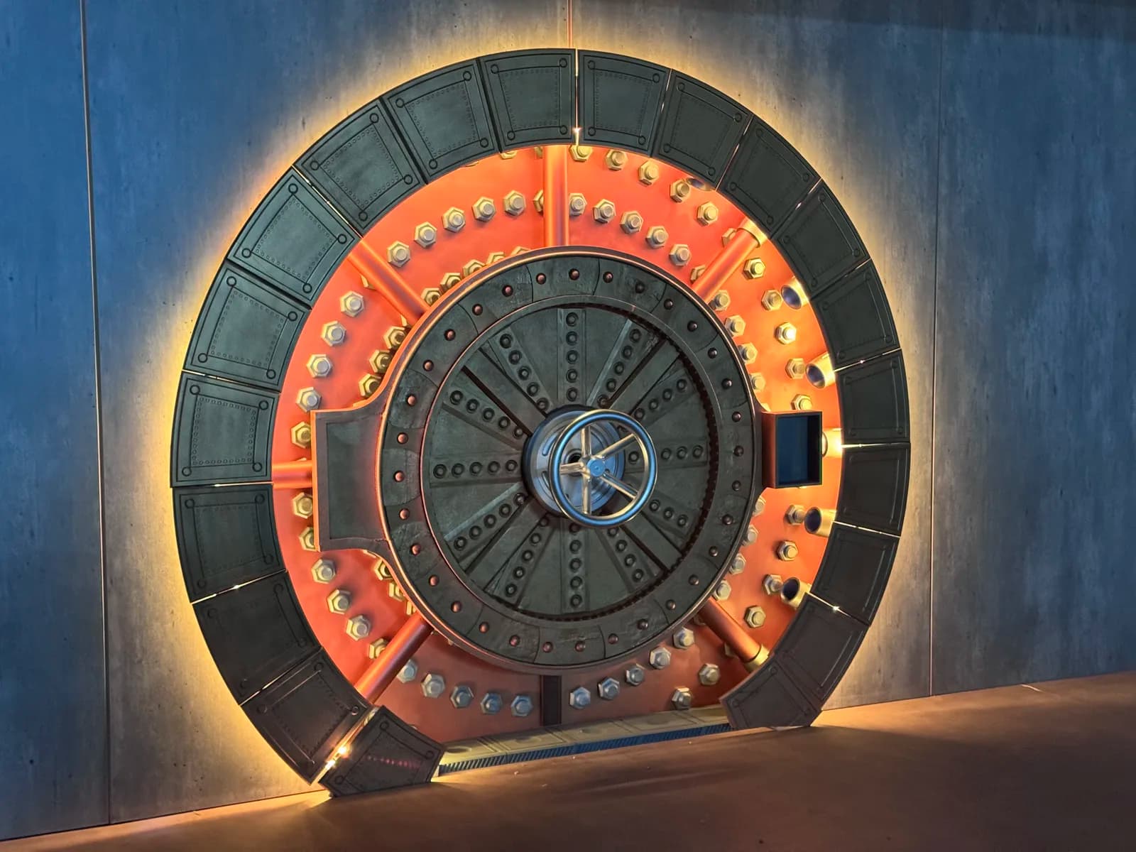 Completed vault door installed in a grey wall with its lights on