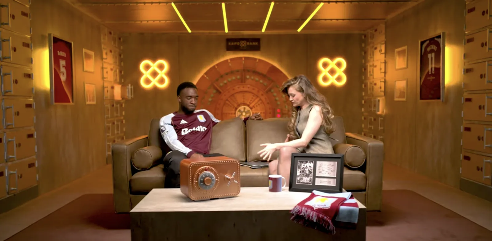 Two presenters on a campaign set with a copper safe and vault door behind them